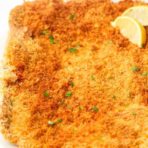 Giant chicken schnitzel on a white plate with lemon wedges and chopped parsley