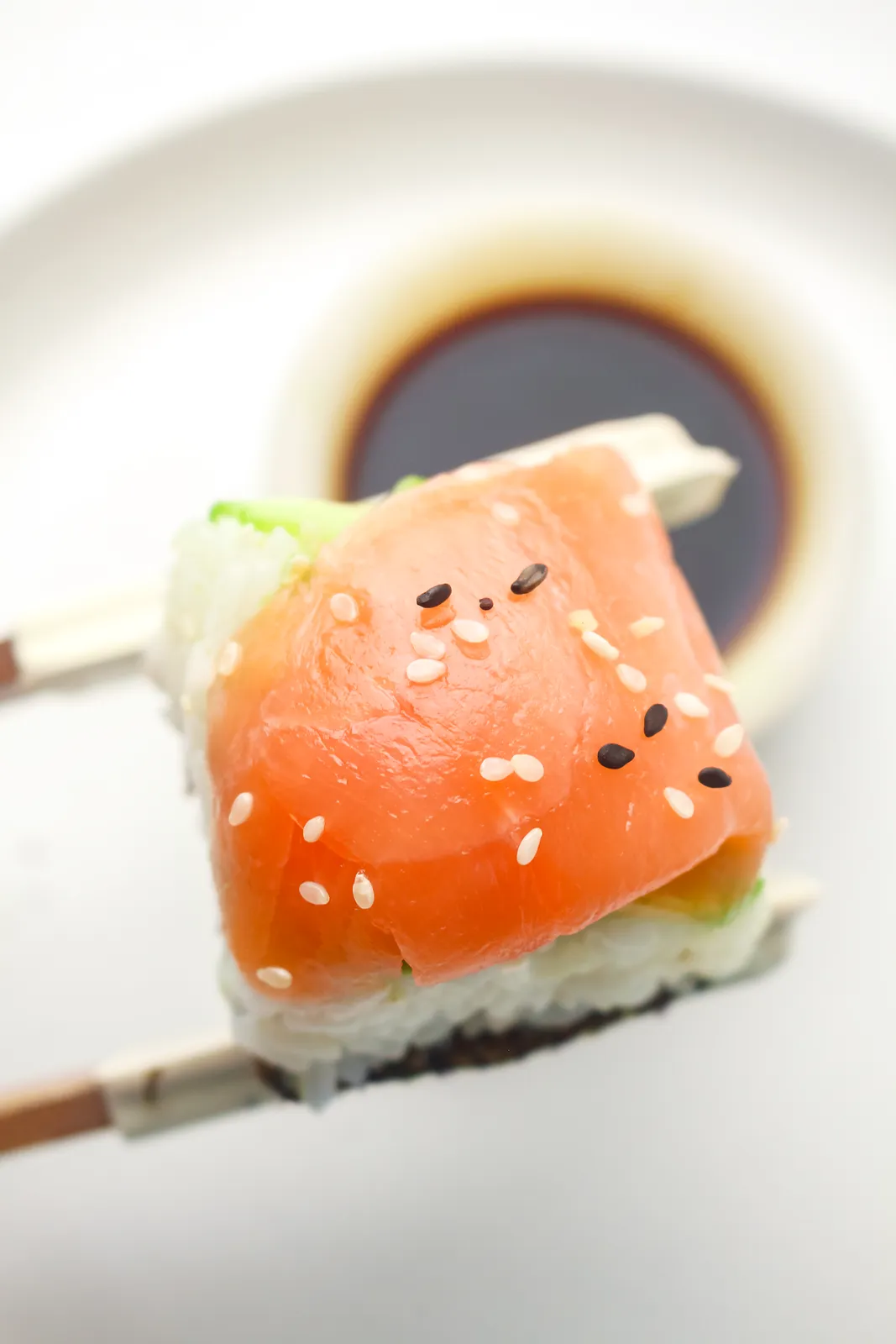 Chopsticks lifting a salmon and rice bite over a small dish of soy sauce