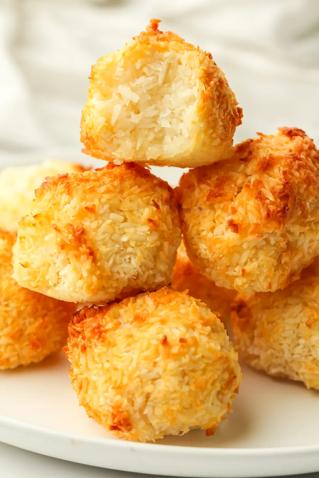 Healthy coconut macaroons piled on a white plate, the top one bitten to show the chewy centre