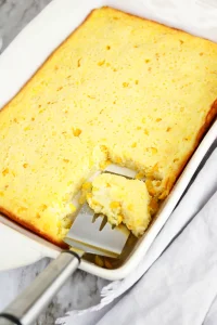 A metal spatula lifting the first creamy scoop from a golden sweetcorn bake