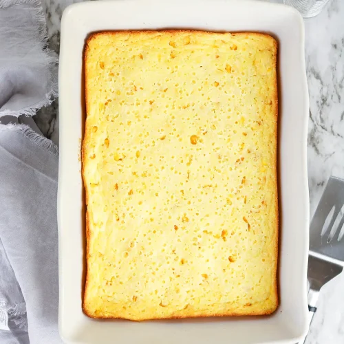Corn souffle baked golden in a white casserole dish on a marble counter