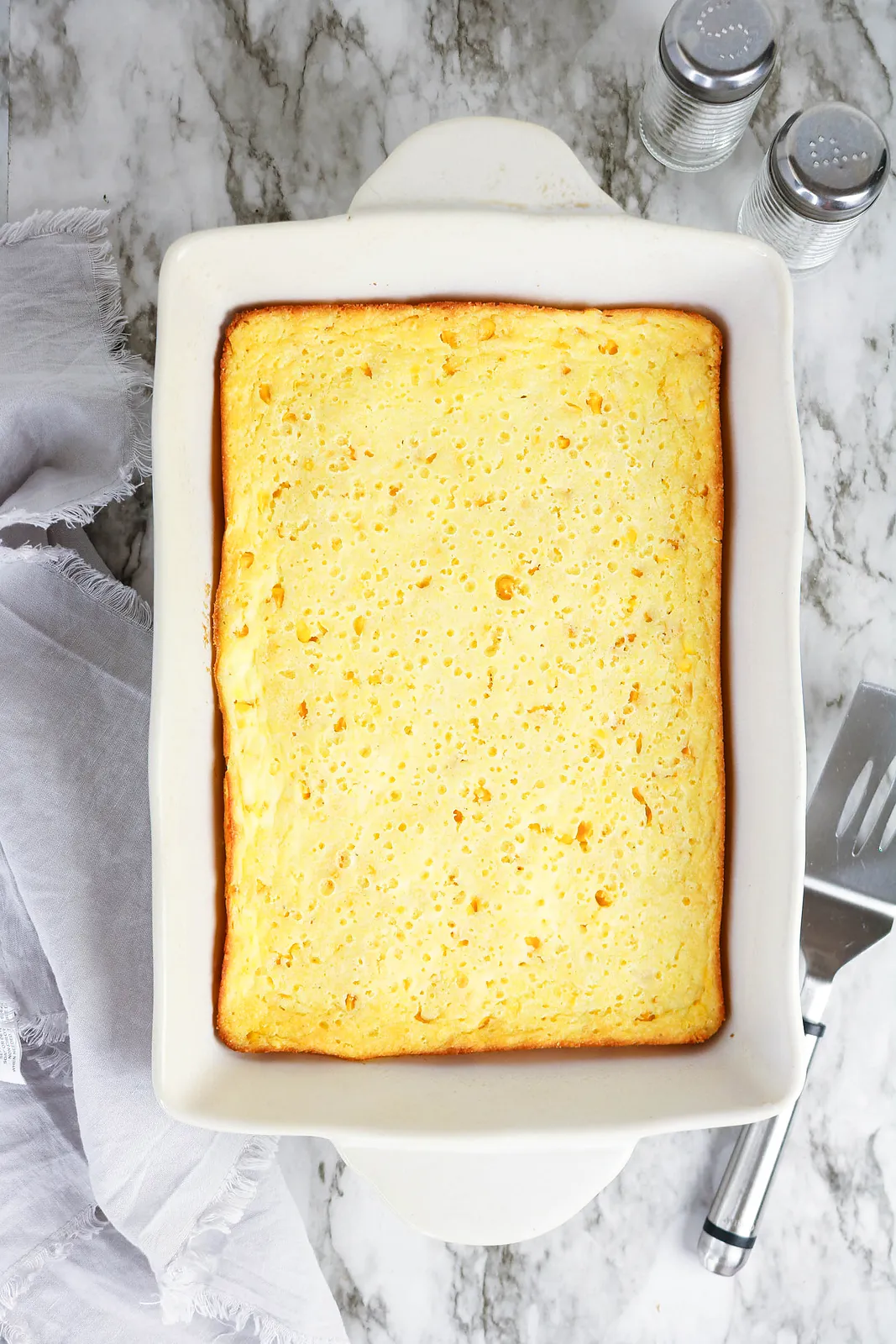 Corn souffle baked golden in a white casserole dish on a marble counter