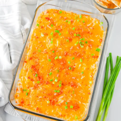 Crack chicken dip baked in a glass dish with melted cheddar, bacon and green onions