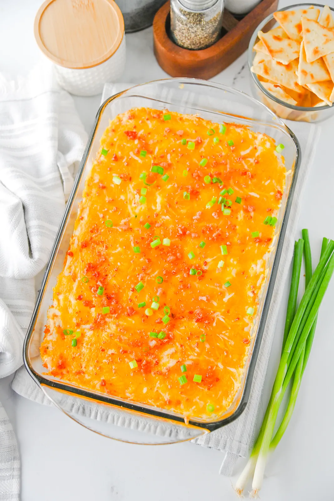 Crack chicken dip baked in a glass dish with melted cheddar, bacon and green onions
