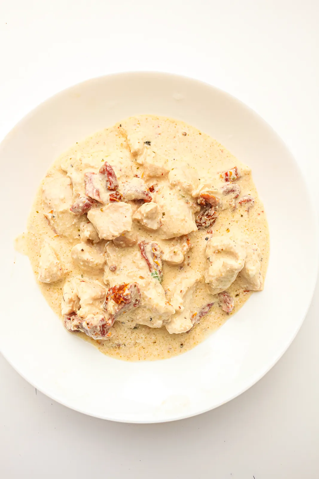 Overhead view of tender diced pieces in a creamy sun-dried tomato sauce in a white bowl