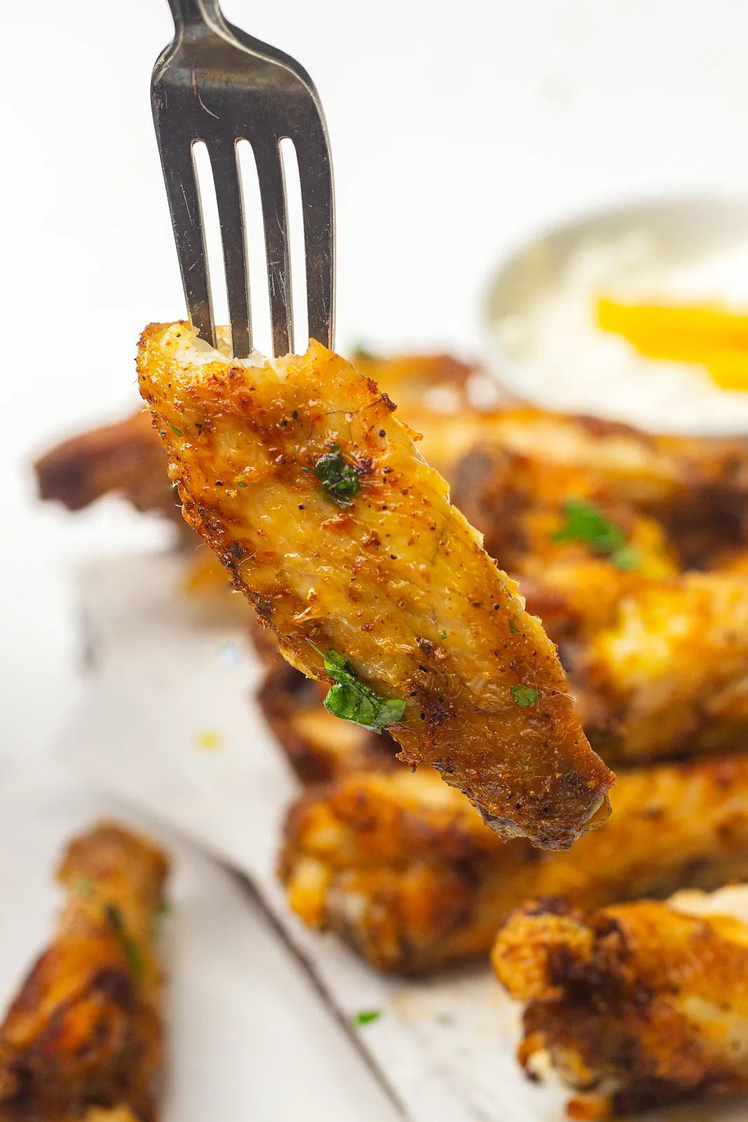 A single crisp wing flat lifted on a fork, with more pieces and a dip behind