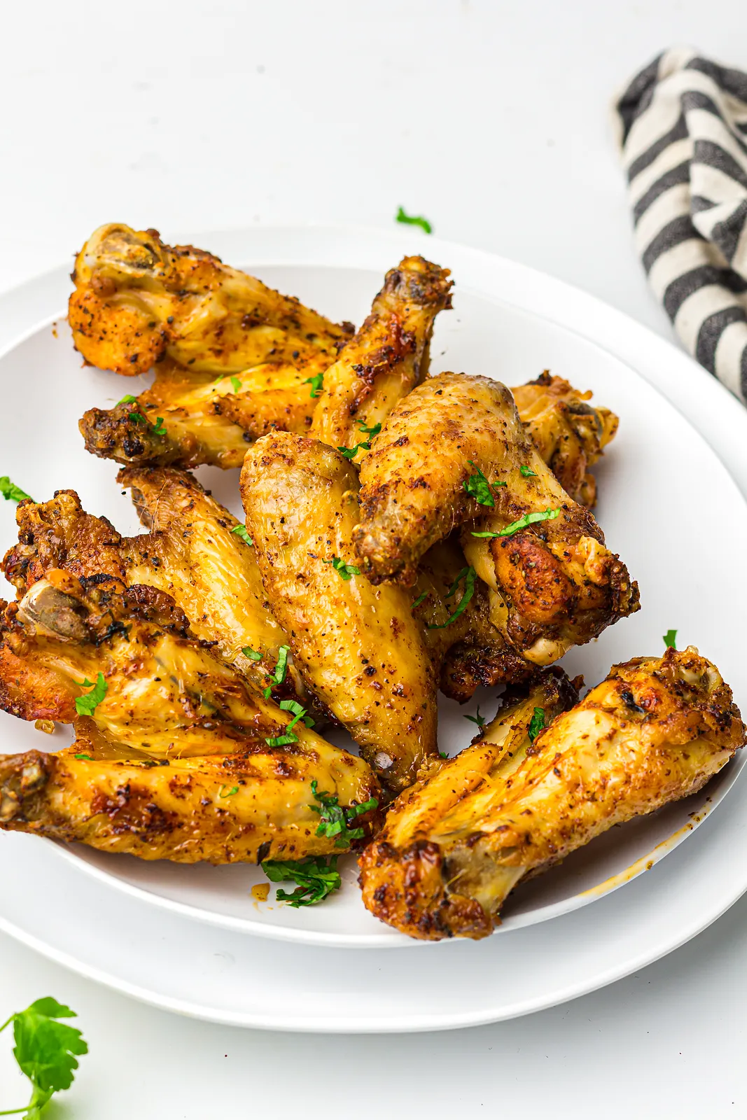 Crispy seasoned wings piled on a white plate with chopped parsley
