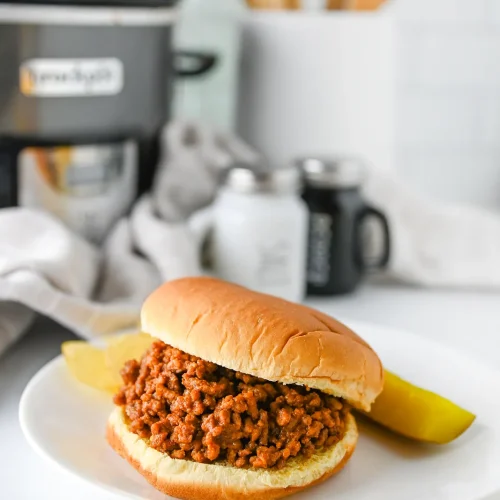 Crock pot sloppy joes in a soft bun with a pickle spear and crisps