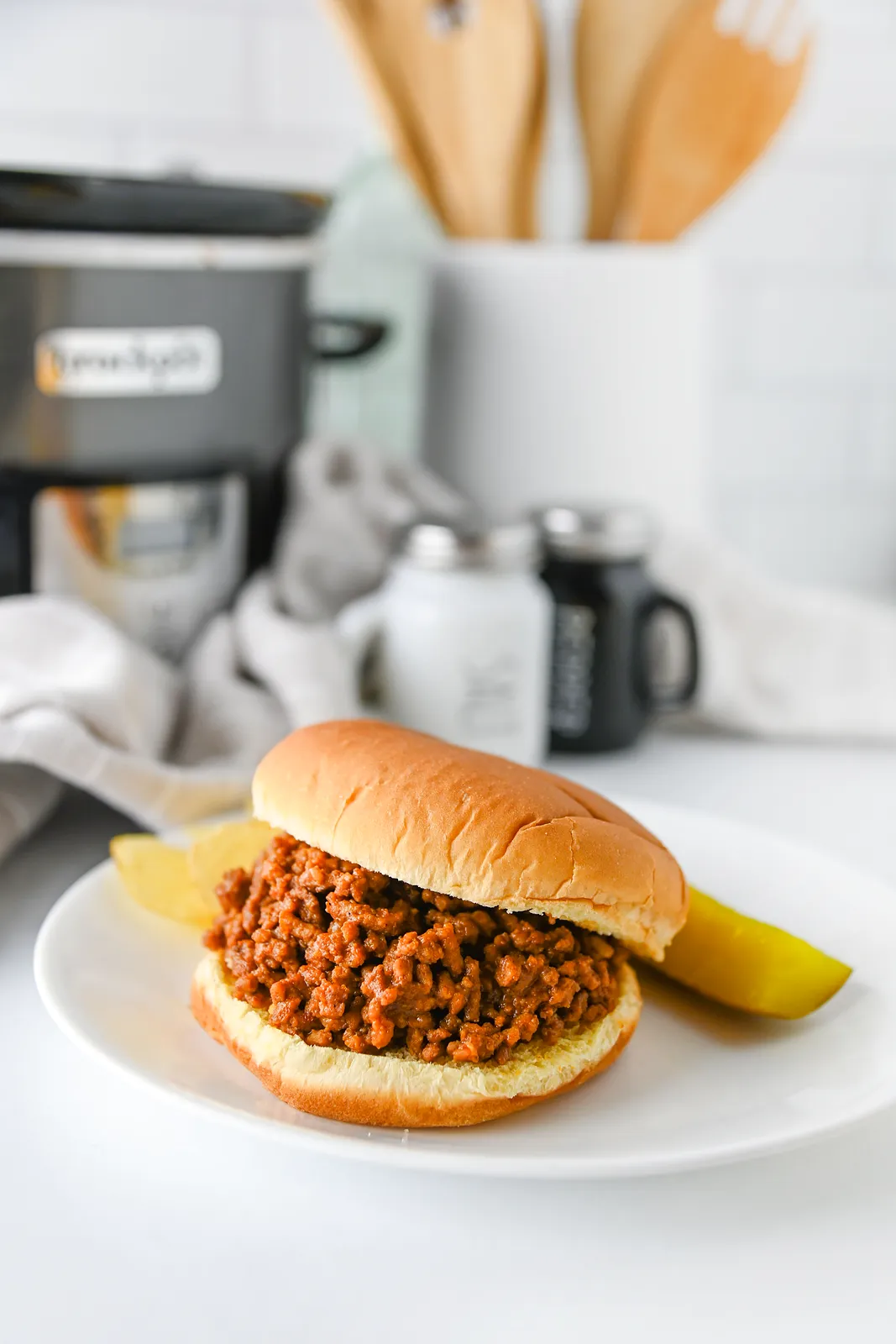 Crock pot sloppy joes in a soft bun with a pickle spear and crisps