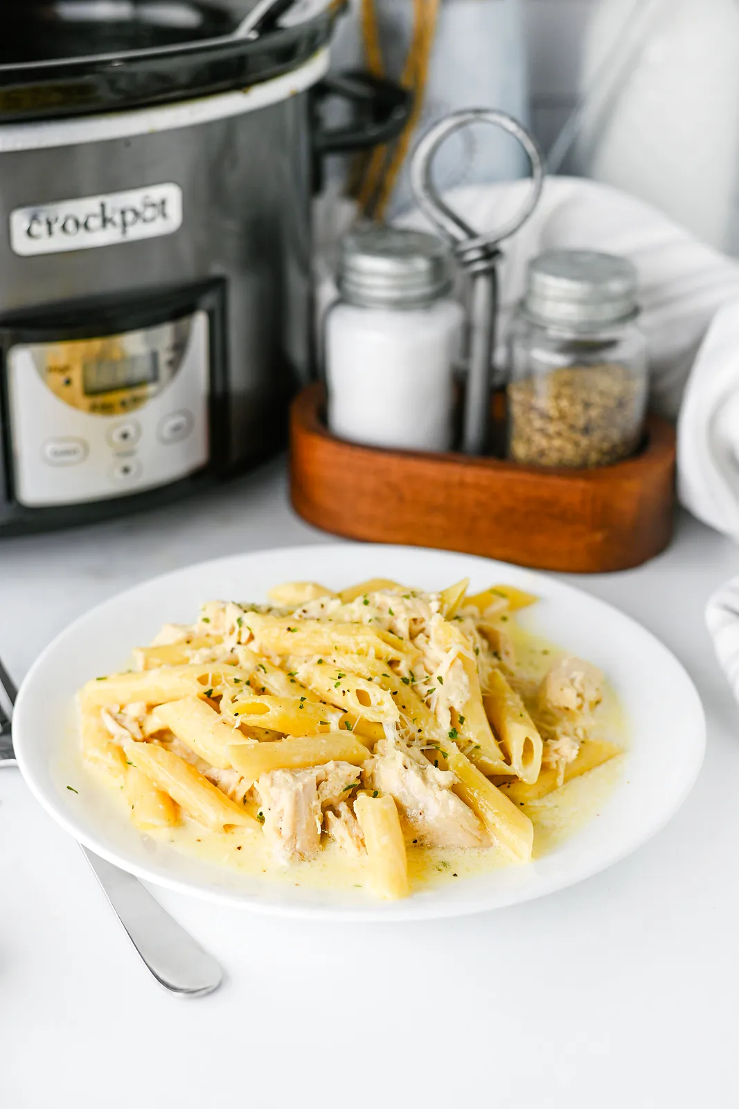 Penne in a creamy Parmesan sauce with shredded chicken on a white plate beside the pot