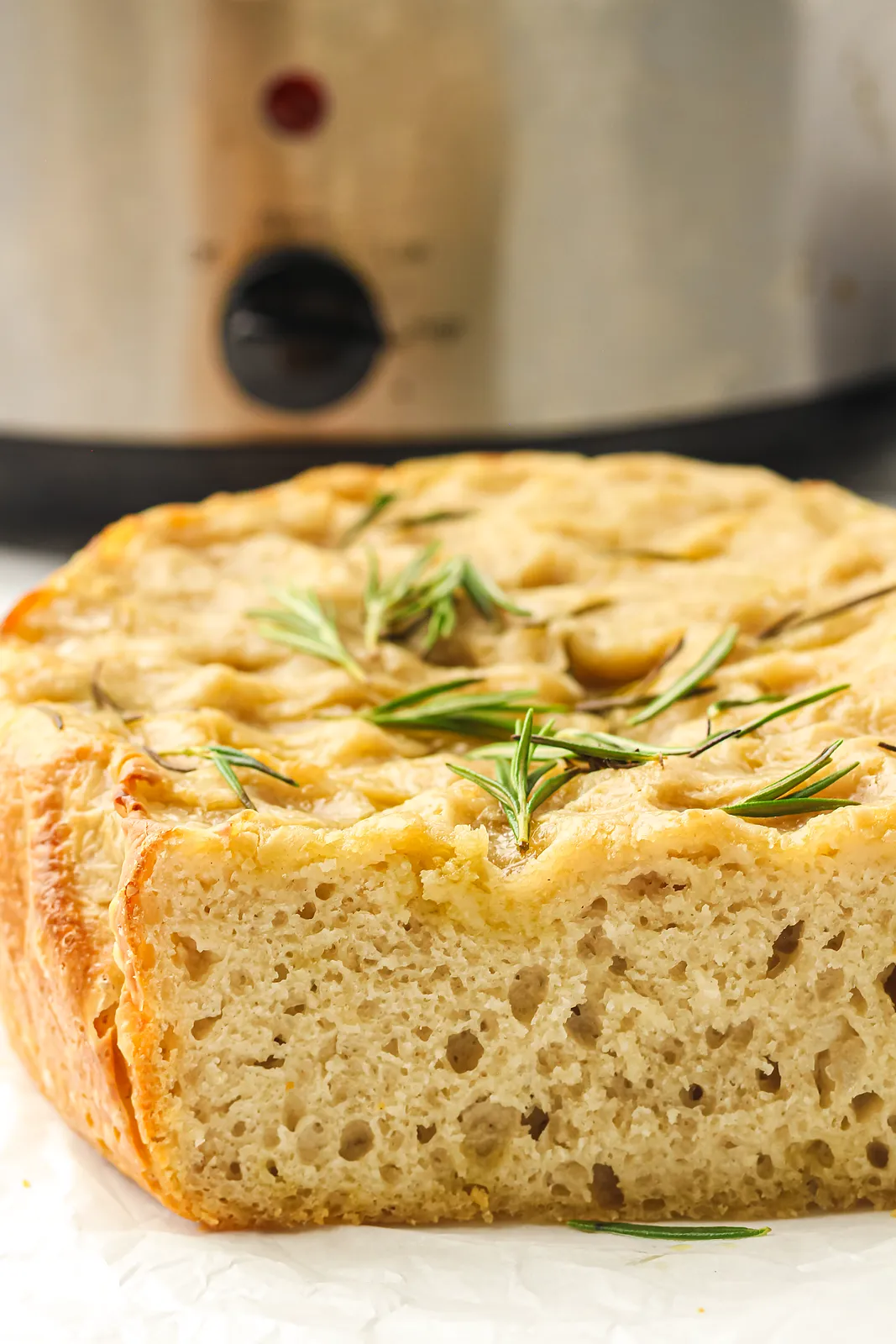 Crockpot focaccia bread with rosemary, sliced to show the airy crumb, in front of a slow cooker