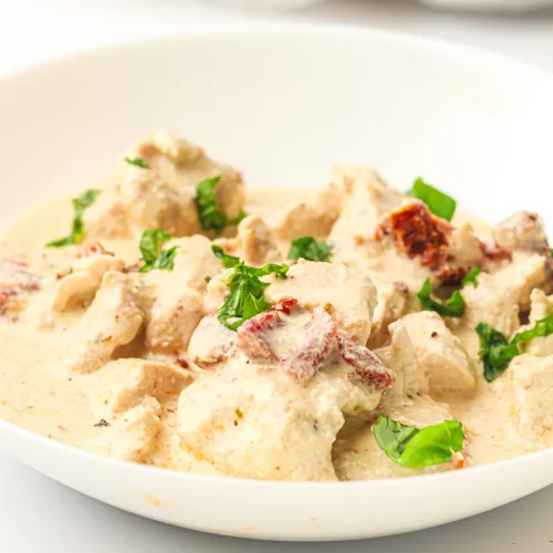 Crockpot marry me chicken in a white bowl with sun-dried tomatoes and fresh basil