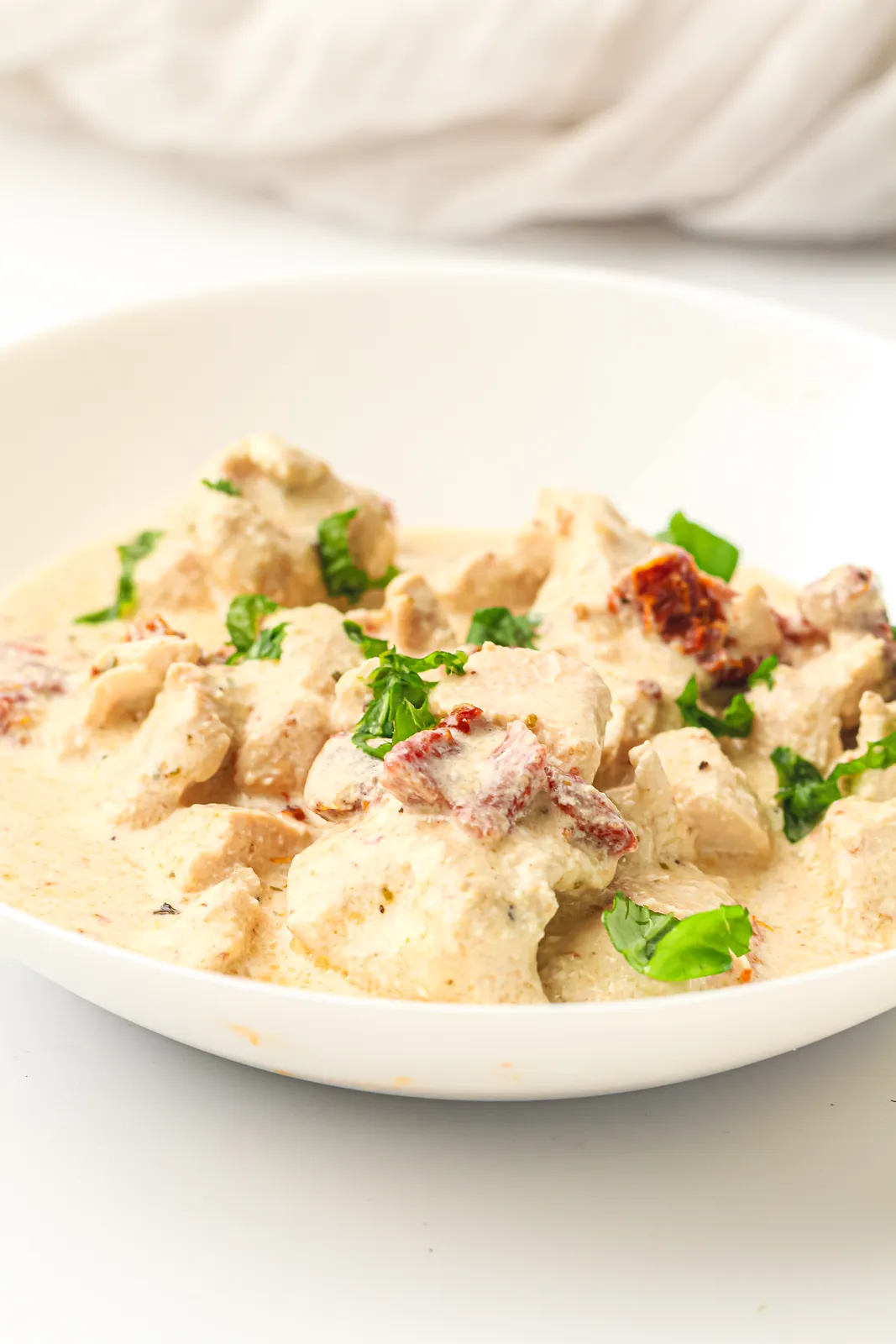Creamy sauce with sun-dried tomatoes and basil over tender diced meat in a white bowl