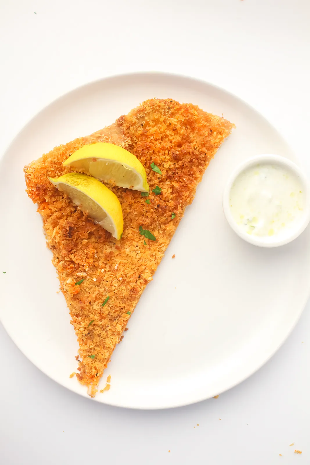 One crunchy triangle on a plate with lemon wedges and a pot of creamy dip