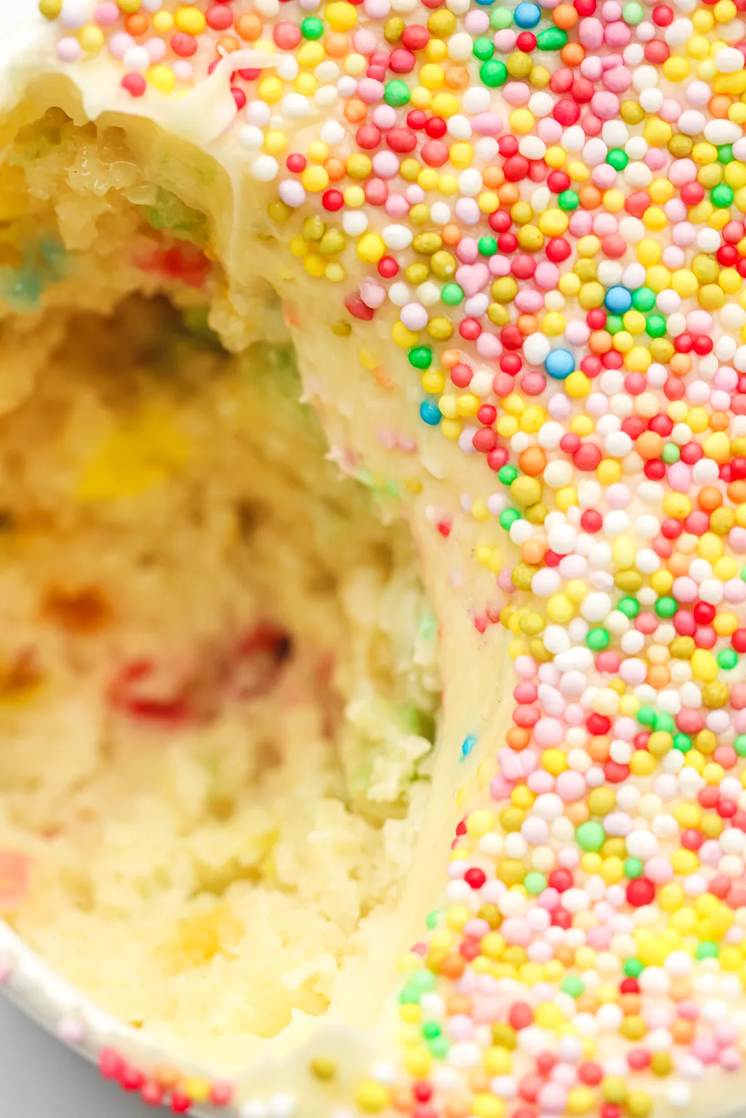 Close up of a scooped cup showing soft sponge, frosting and coloured sprinkles