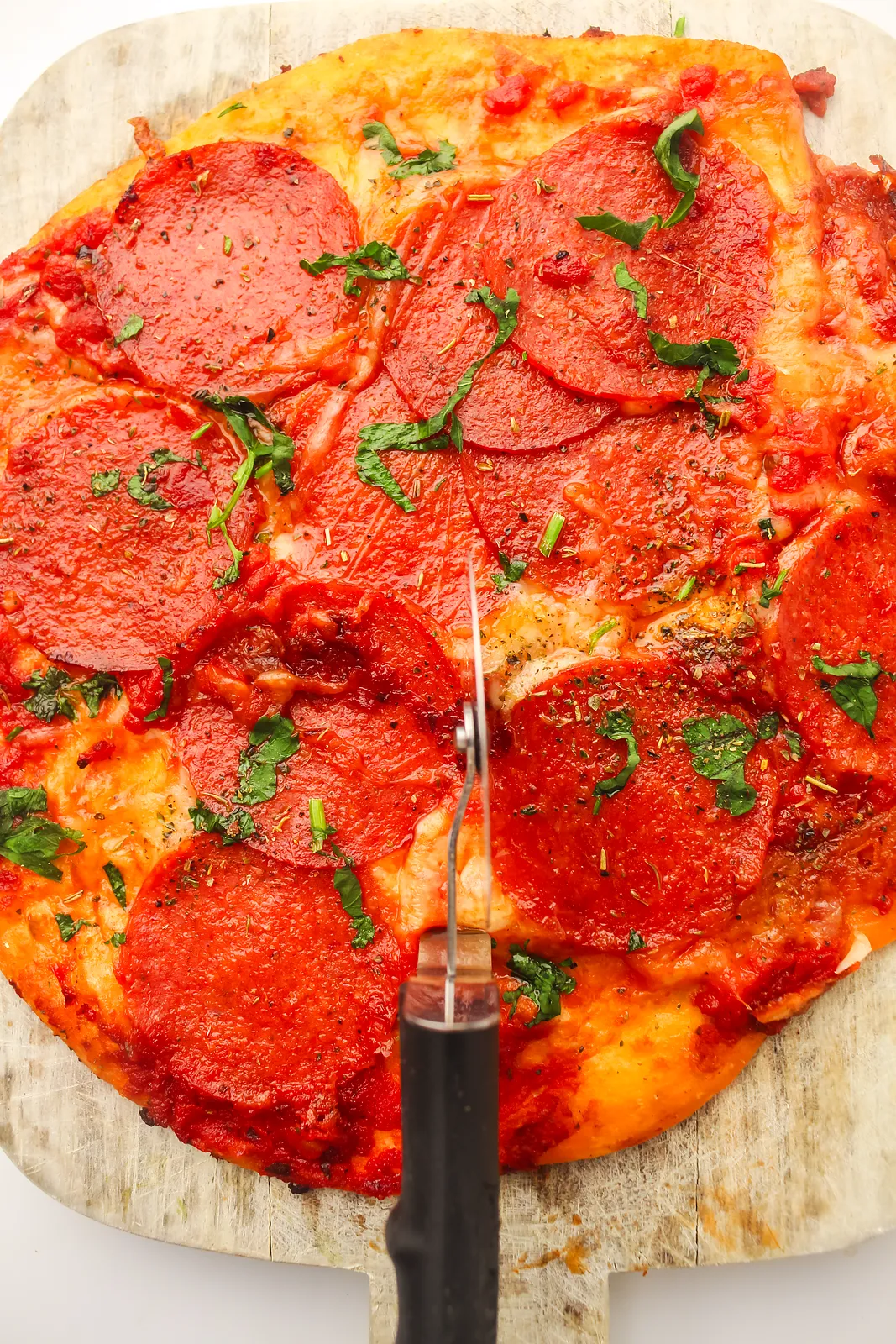 Cutting a crispy pepperoni flatbread into wedges with a wheel on a wooden board