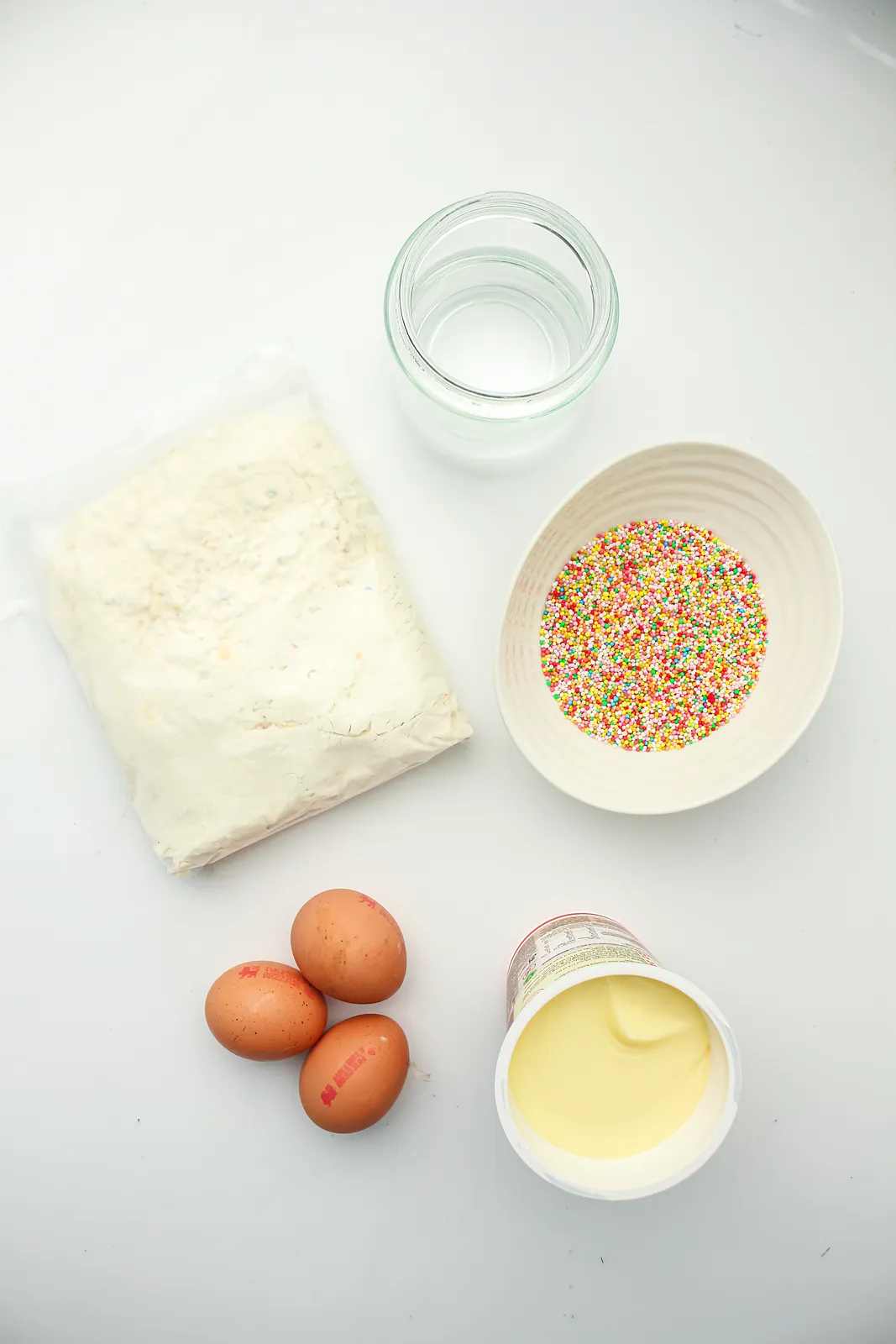 Ingredients for a dot cake: funfetti cake mix, eggs, oil, vanilla frosting and rainbow sprinkles