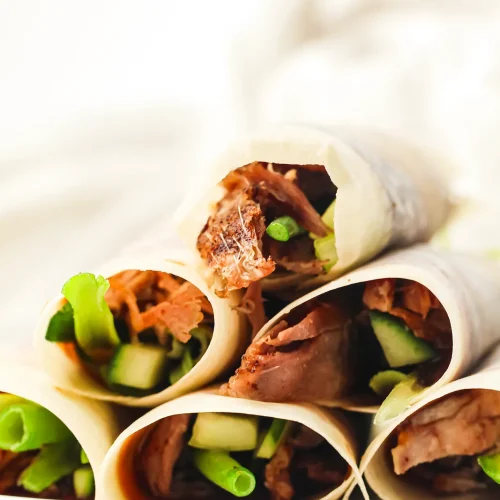 Duck pancakes rolled with hoisin, cucumber and spring onion on a white plate