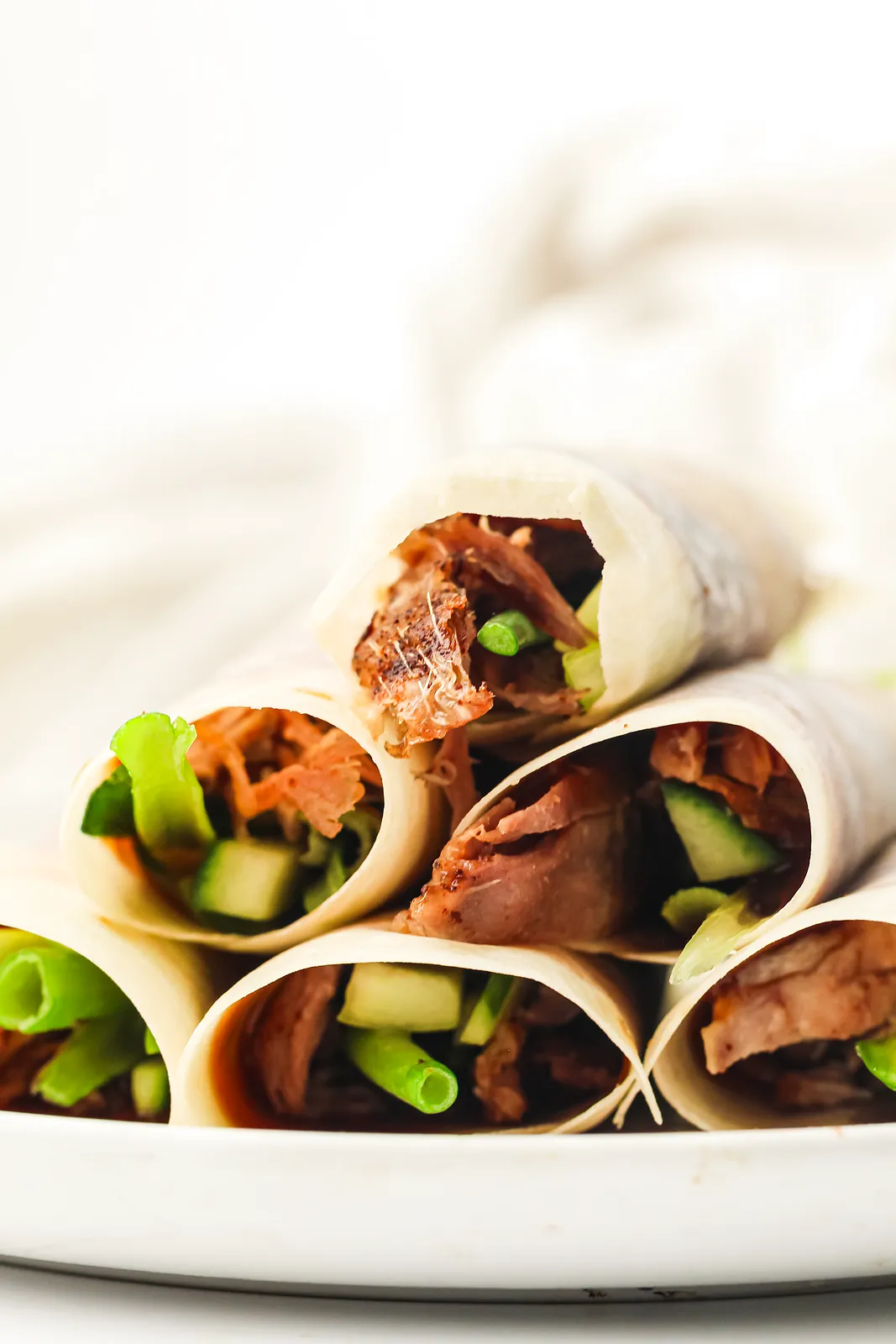 Duck pancakes rolled with hoisin, cucumber and spring onion on a white plate