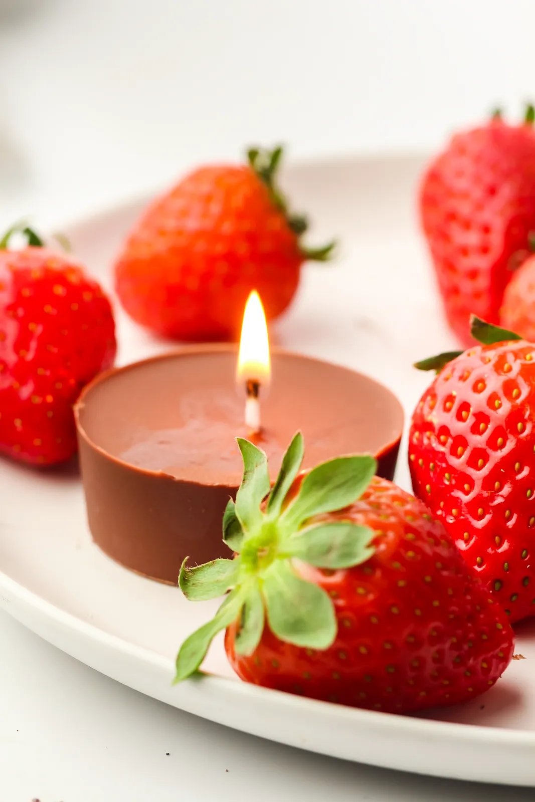 Edible chocolate candles lit on a white plate with fresh strawberries