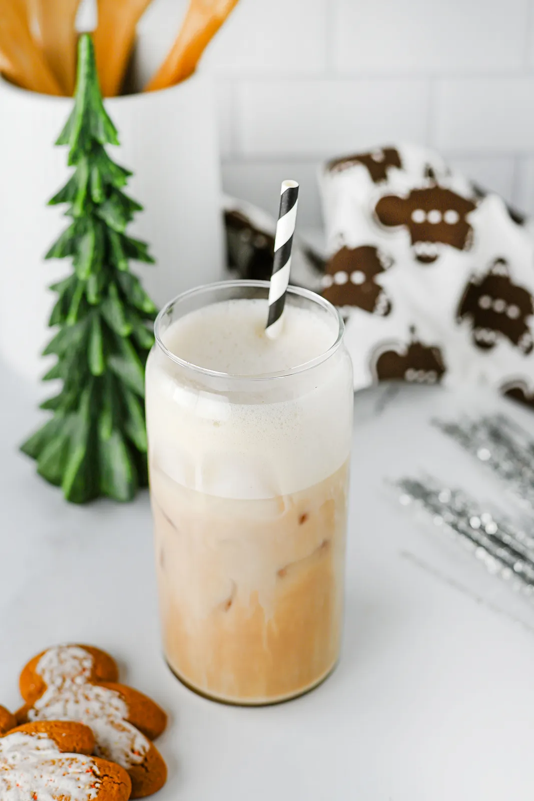 A festive iced latte with a black and white straw, a little green tree and iced gingerbread men