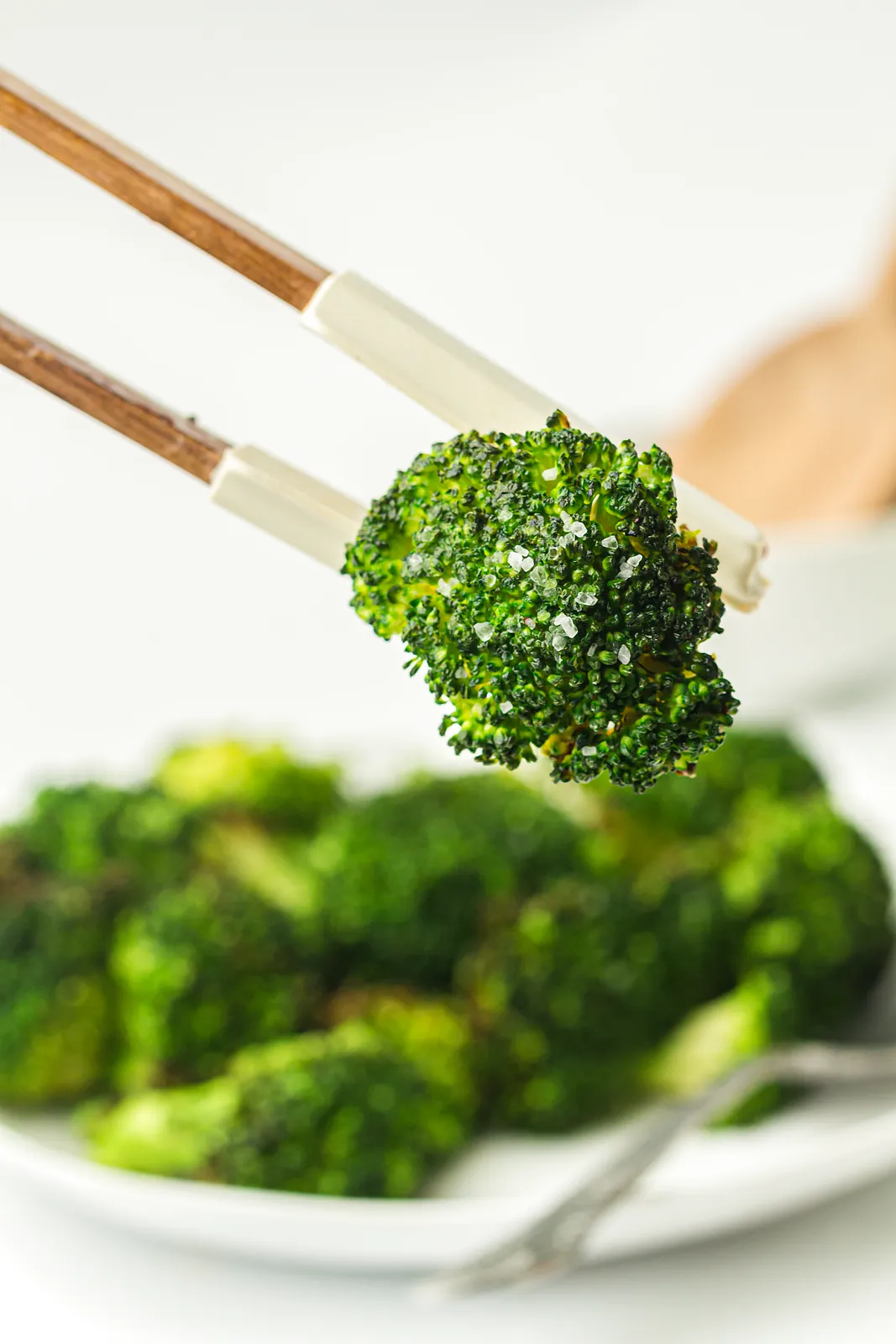 A single charred floret with flaky salt lifted from the plate with wooden tongs