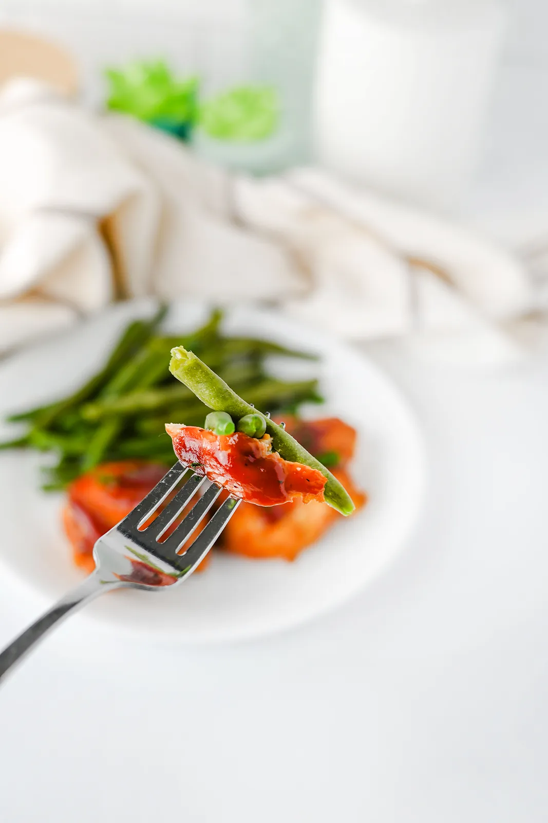 A forkful of tender, sauce coated meat and a green bean lifted from the plate