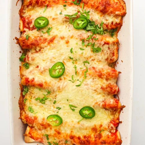 Freezer enchiladas baked golden in a white dish with jalapeño slices and coriander