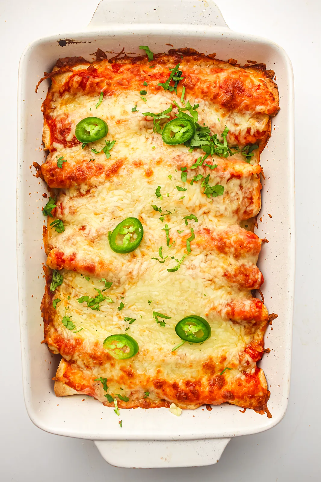 Freezer enchiladas baked golden in a white dish with jalapeño slices and coriander