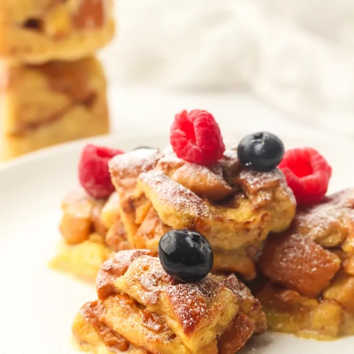 Freezer French toast brioche bites on a plate with raspberries, blueberries and a dusting of icing sugar