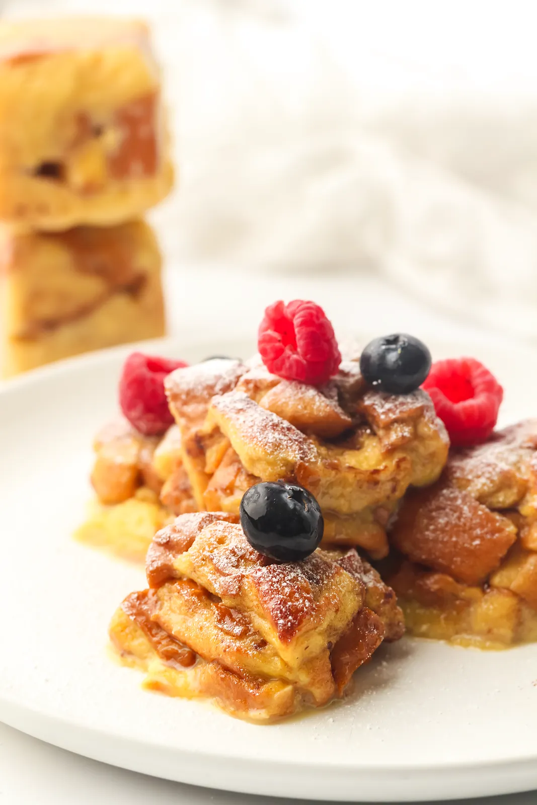 Freezer French toast brioche bites on a plate with raspberries, blueberries and a dusting of icing sugar