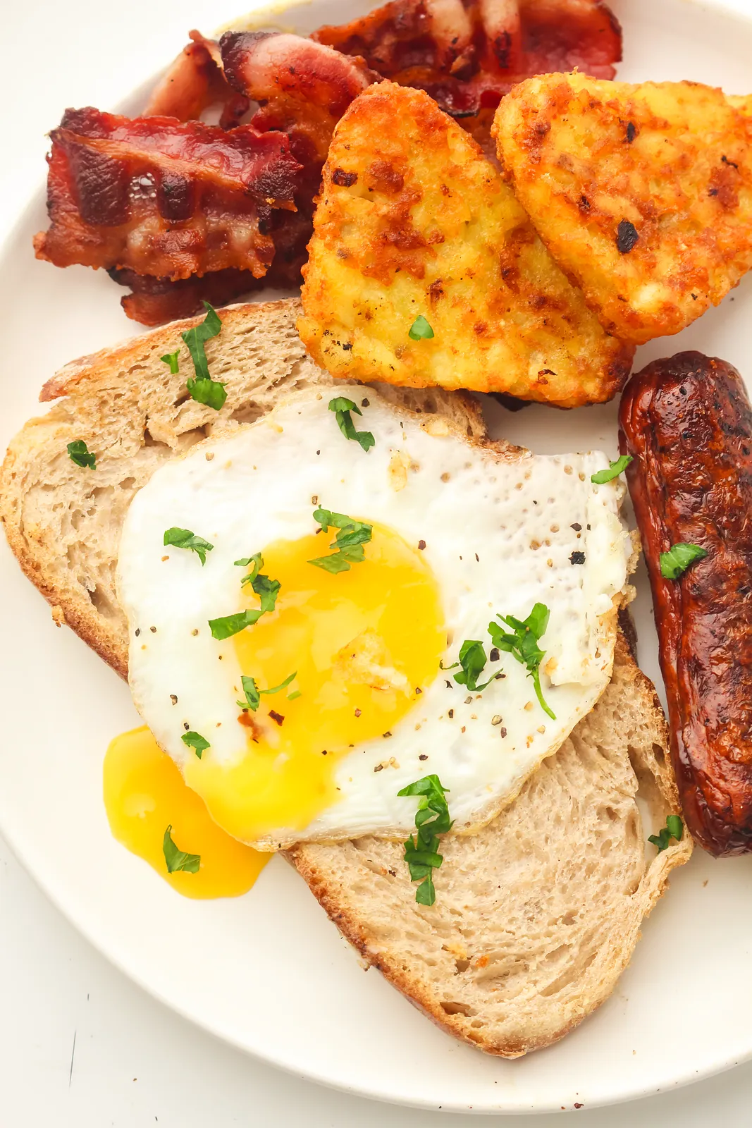 A sunny side up egg with parsley on toast next to golden potato triangles and a sausage