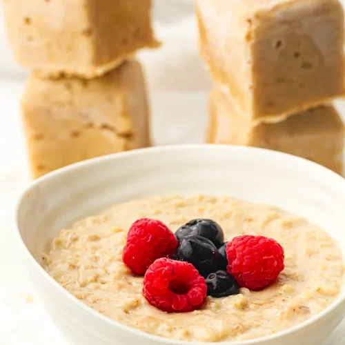 Frozen oatmeal cubes stacked beside a bowl of creamy porridge topped with raspberries and blueberries