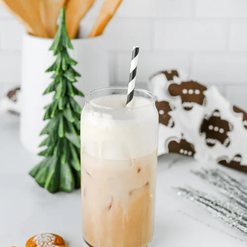 Iced gingerbread chai in a tall glass with oat milk foam, a striped straw and gingerbread biscuits