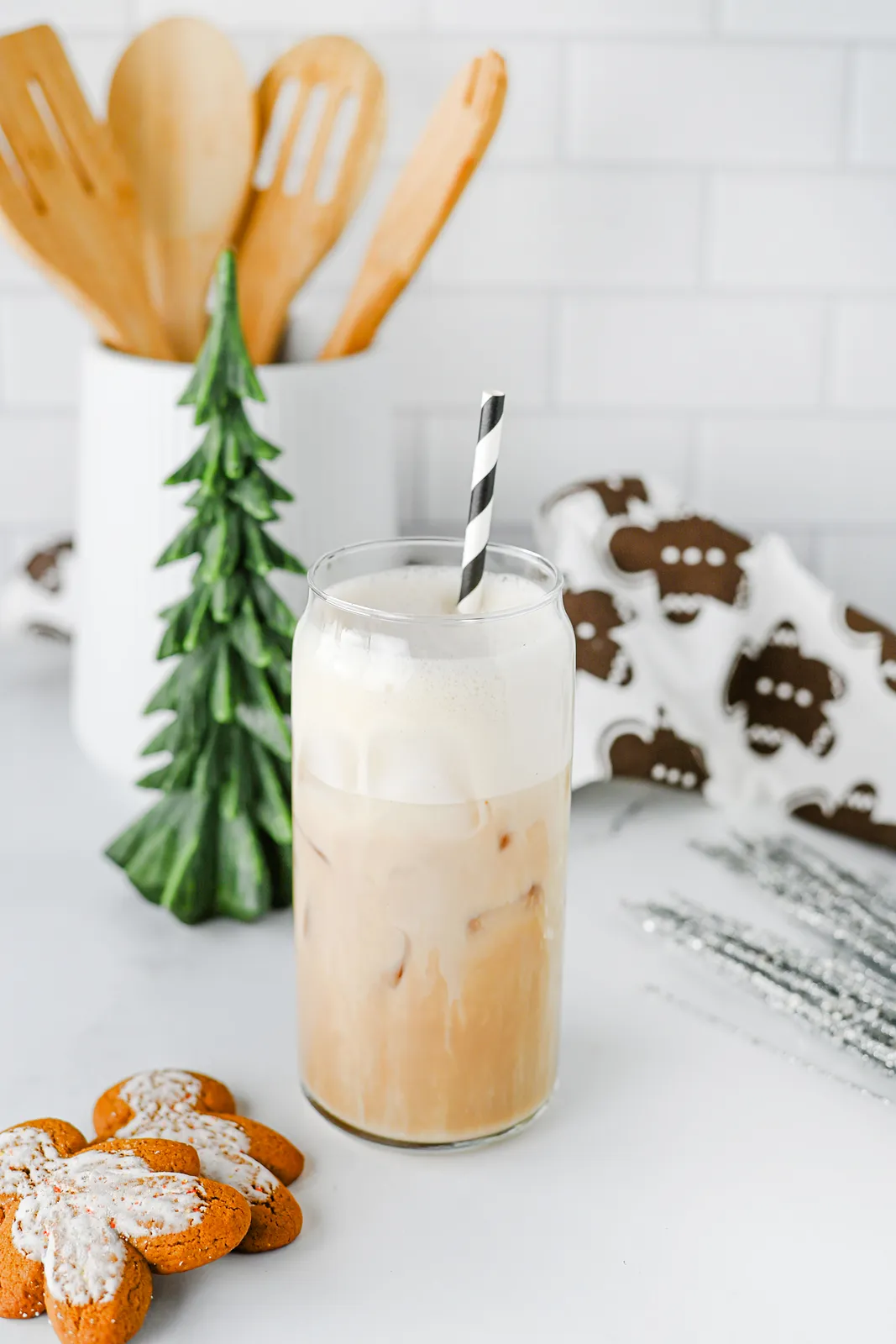 Iced gingerbread chai in a tall glass with oat milk foam, a striped straw and gingerbread biscuits