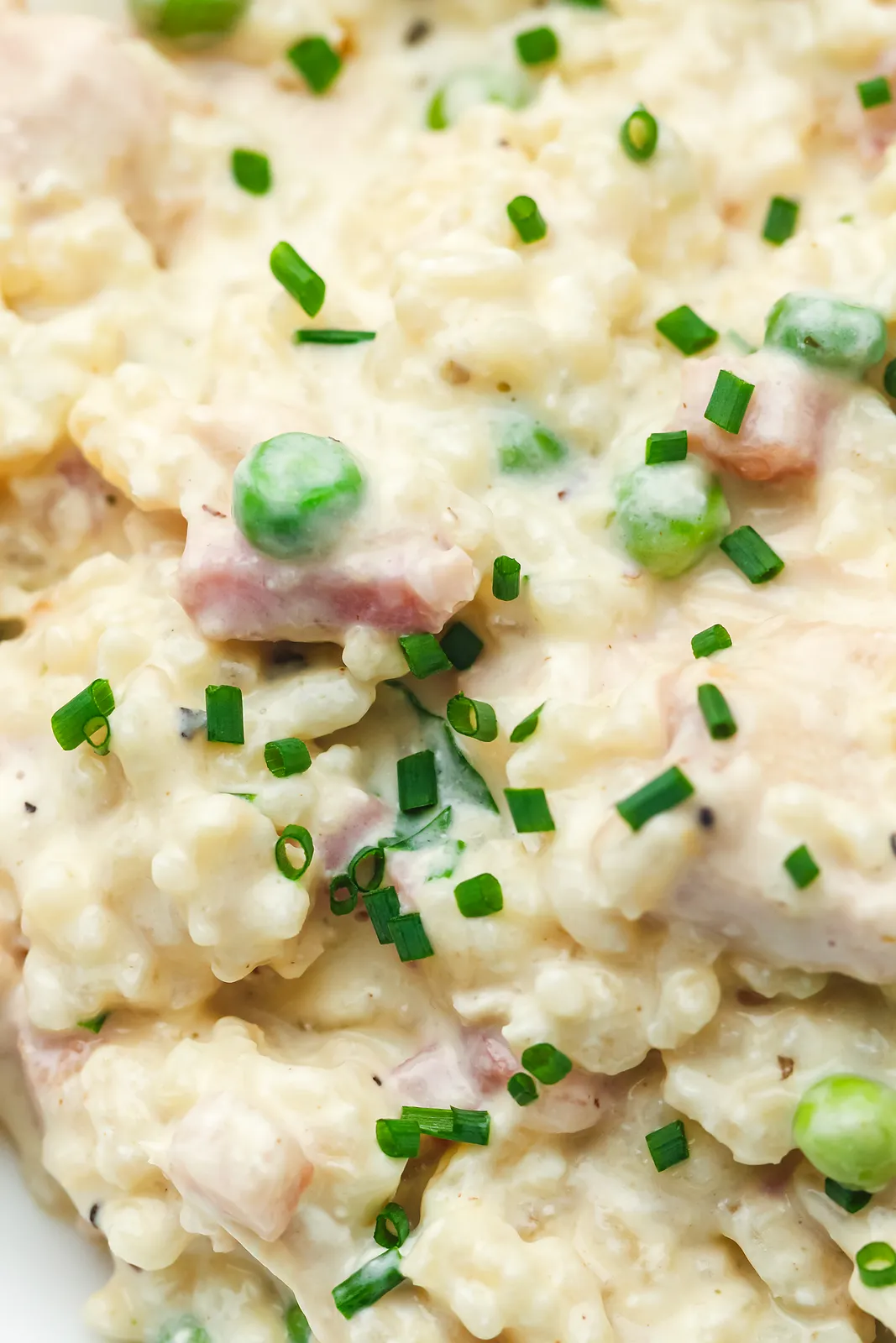 Close up of glossy creamy rice with sweet peas and snipped chives