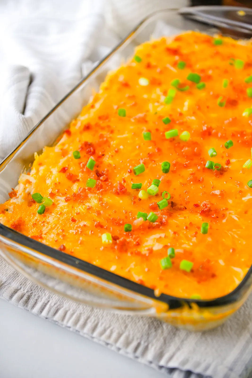 Close up of a golden, bubbling cheddar topping scattered with bacon bits and sliced spring onion