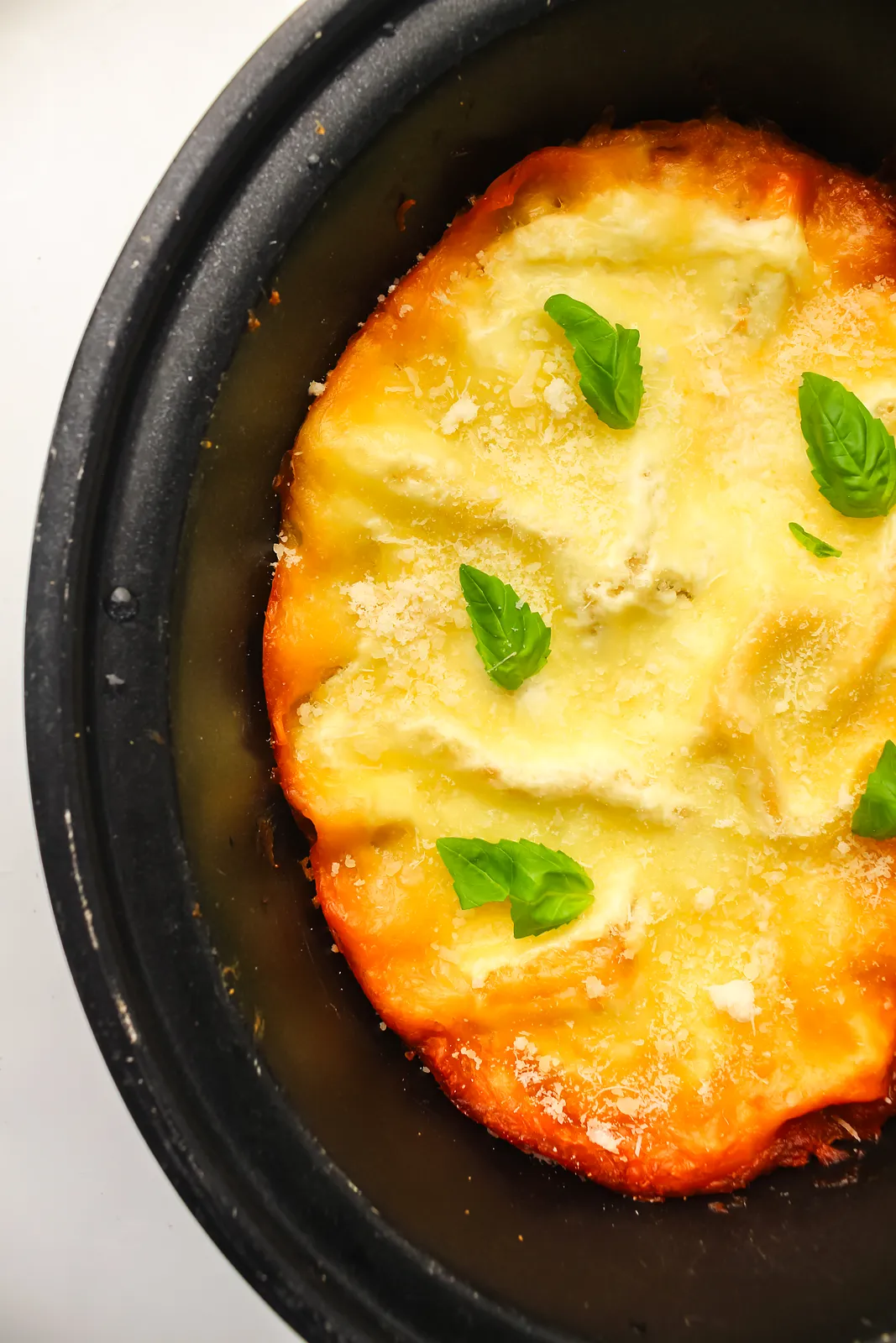 Golden melted mozzarella and basil leaves covering the whole pot, seen from above
