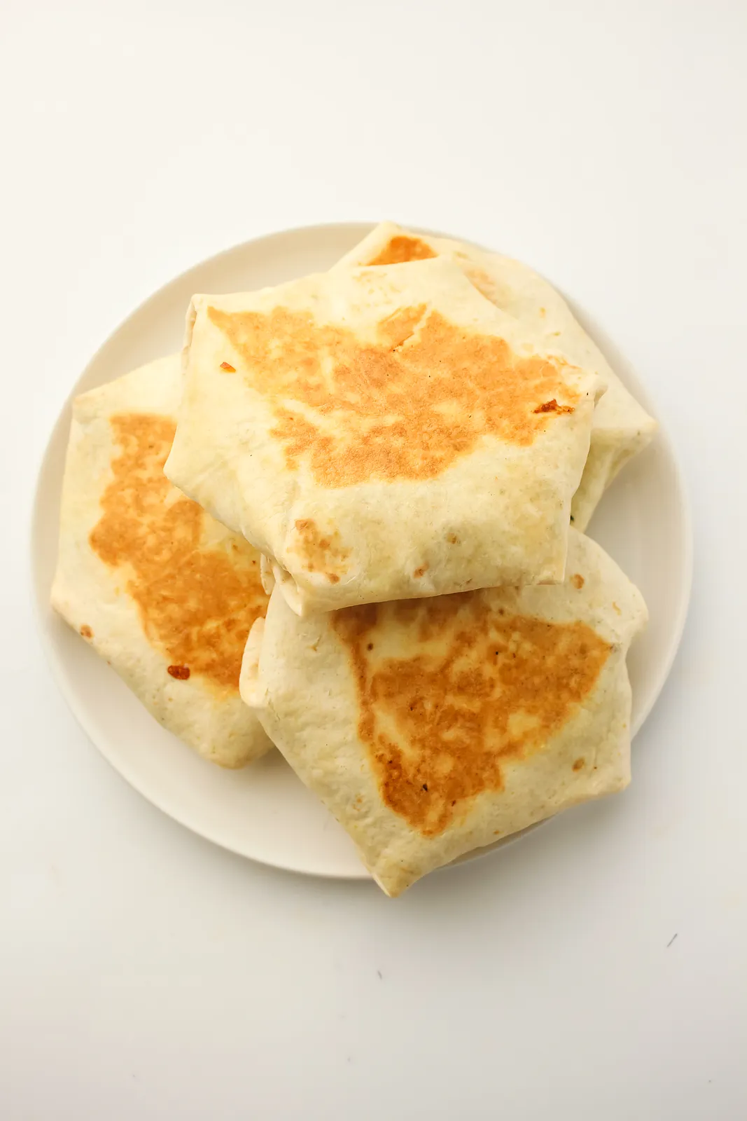 Golden folded tortilla parcels piled on a round white plate seen from above
