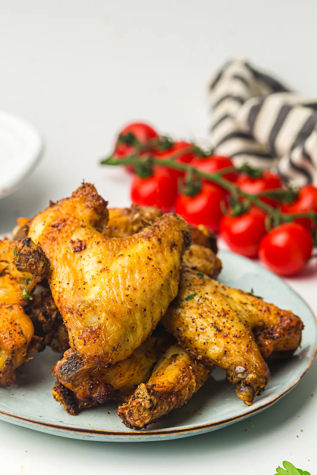 Golden wings on a pale blue plate with a vine of cherry tomatoes behind