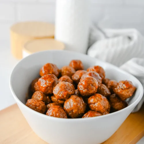 Grape jelly meatballs in a white bowl on a wooden board