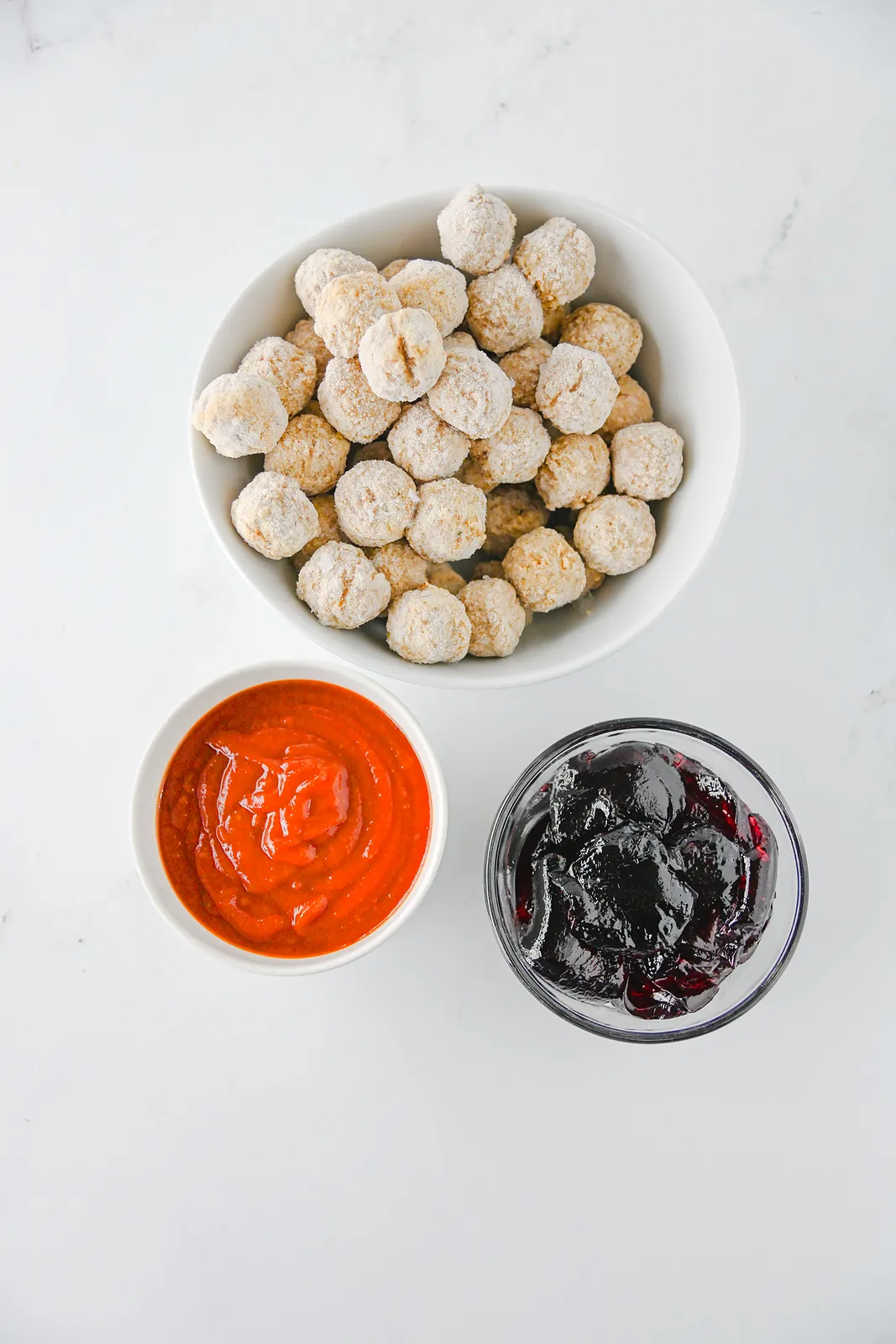 Ingredients for grape jelly meatballs: frozen meatballs, chili sauce and grape jelly in bowls