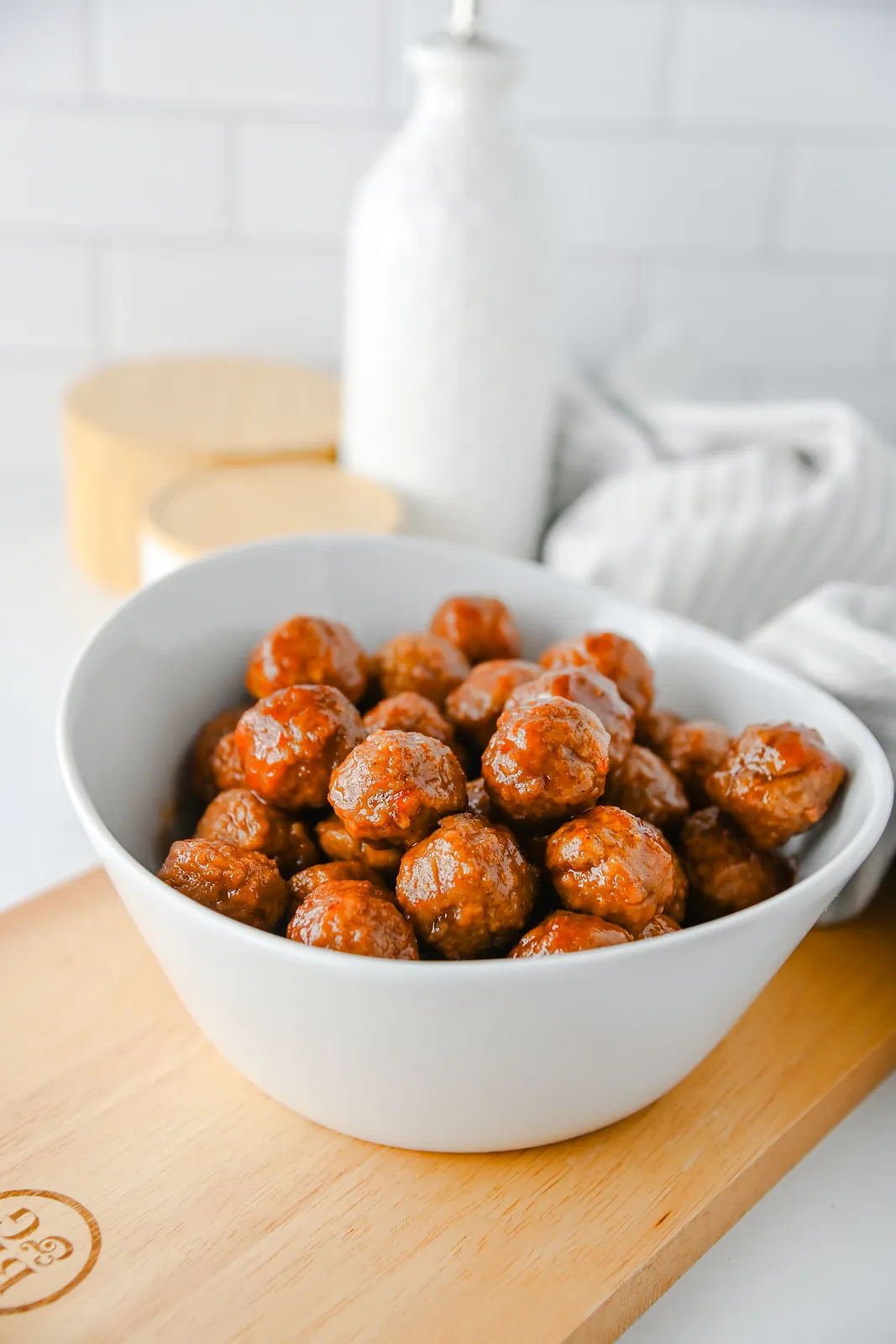 Grape jelly meatballs in a white bowl on a wooden board