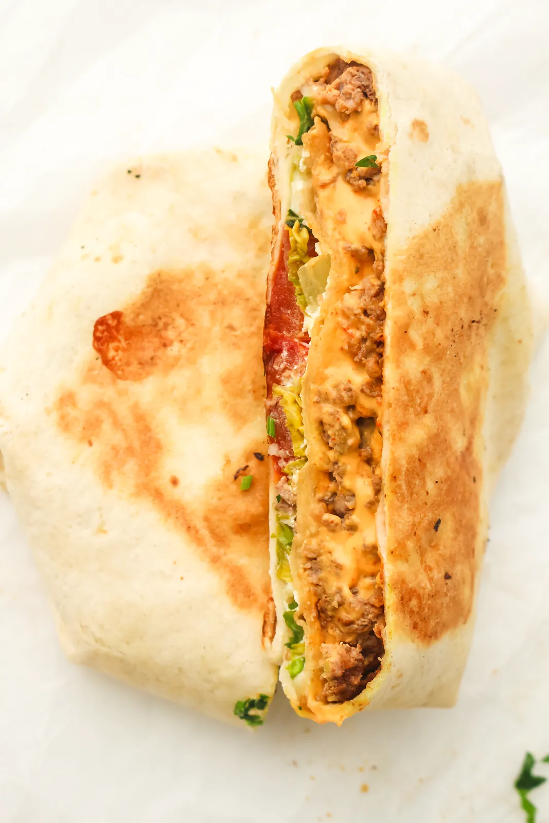 A golden tortilla parcel cut in half and stood upright to show the beef, cheese and salad layers