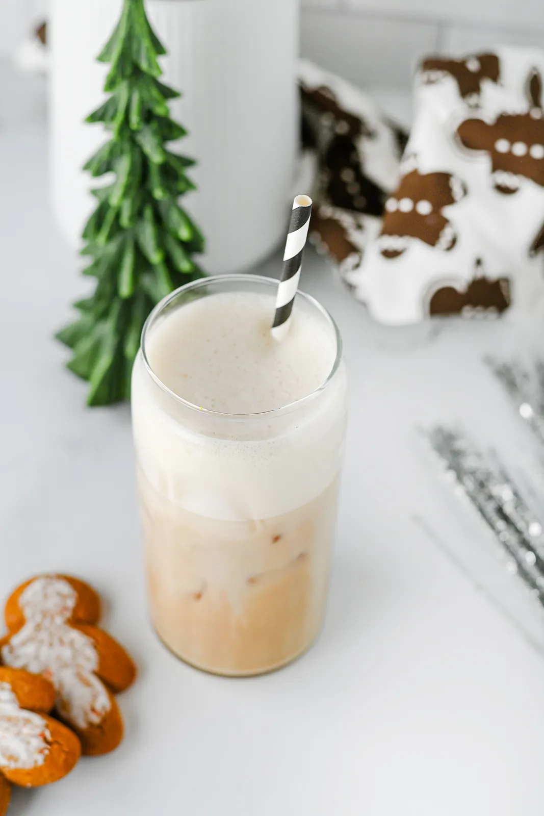 A frothy holiday drink in a tall glass beside silver tinsel and gingerbread print linen