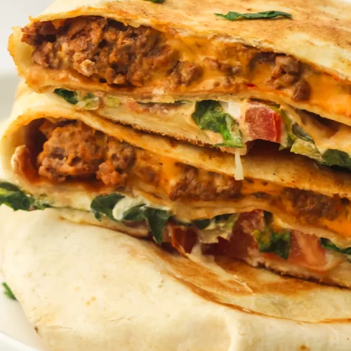 Homemade crunchwrap halves stacked on a plate showing taco beef, nacho cheese, lettuce and tomato