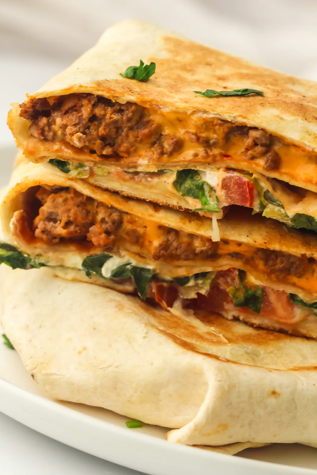 Homemade crunchwrap halves stacked on a plate showing taco beef, nacho cheese, lettuce and tomato