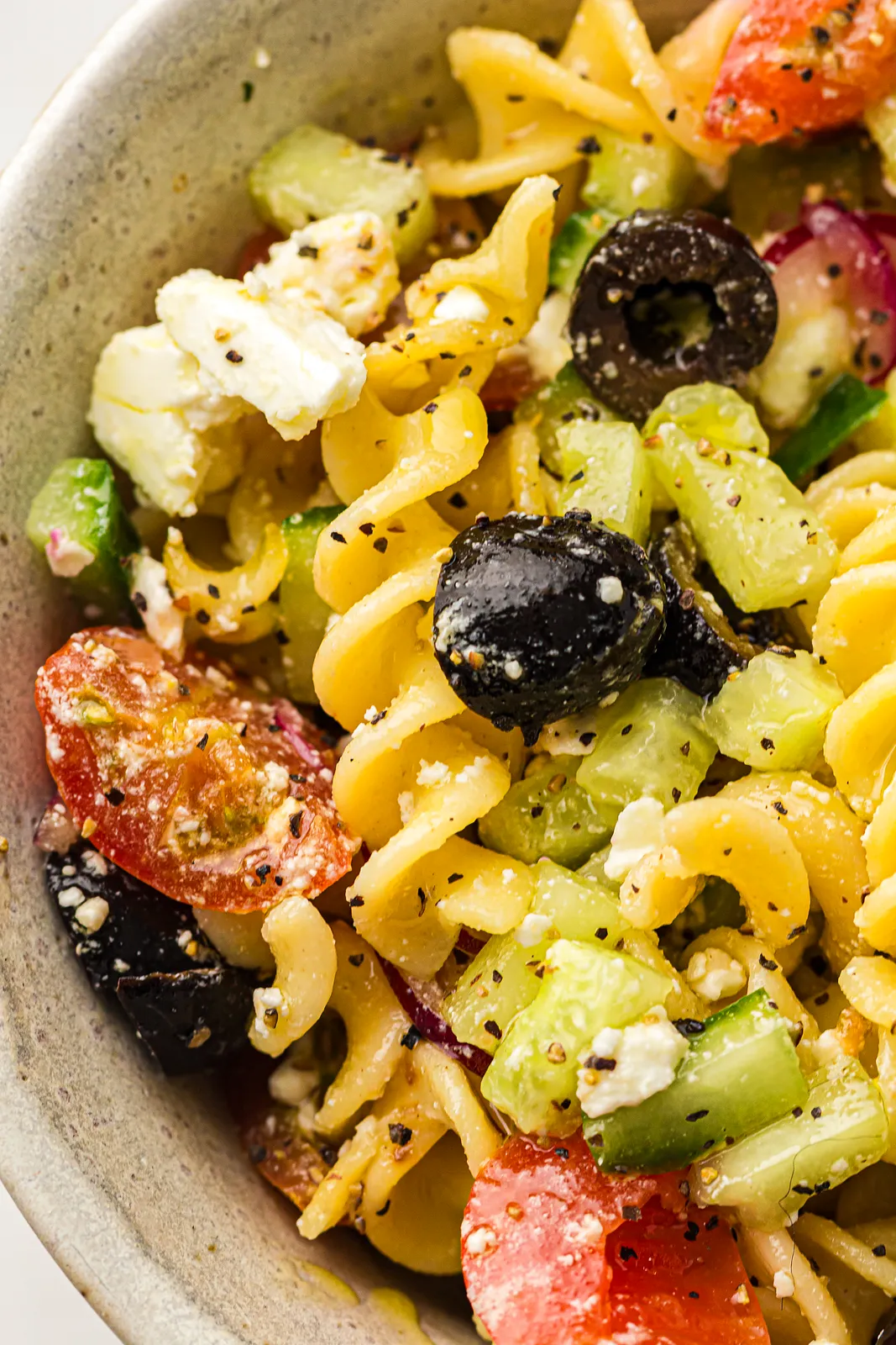 Close up of a whole black olive, feta crumbs and diced cucumber among golden spirals