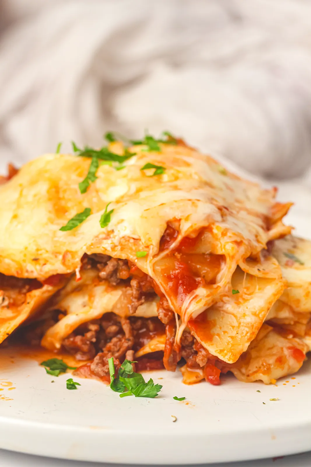 Side view of soft pasta layers and beef ragu under melted cheese on a plate