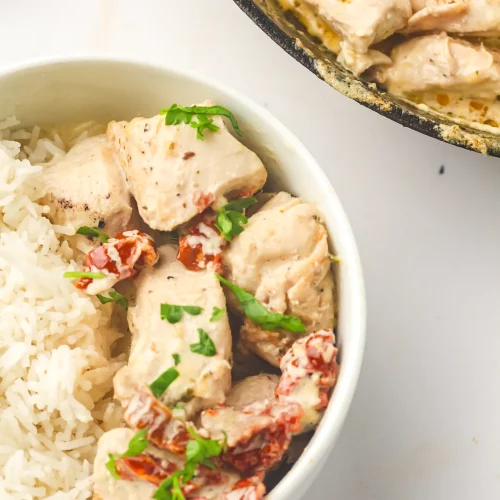 Marry me chicken over white rice in a bowl with the cast iron skillet behind